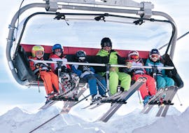 An instructor is sitting in the chair lift with 5 little skiers during kids ski lessons for intermediates.