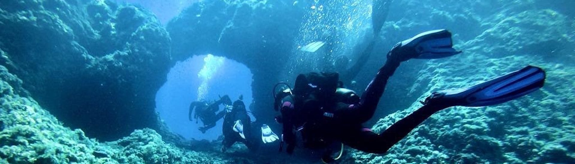 Three divers dive through a cave during the PADI Scuba Diver course in Cala Bona for beginners with Albatros Diving Mallorca.