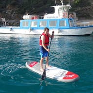 Ein Teilnehmer hat Spaß beim Paddeln vor einem Boot durch die Bucht von Alcúdia bei einem SUP-Board-Verleih in Alcanada Beach mit North Coast Adventure Mallorca.