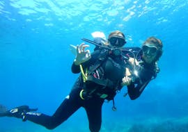 Twee vrouwen onder water met duikuitrusting lachen naar de camera tijdens de proefduik in Sardinië bij Santa Maria Navarrese met Nautica Sea Service.