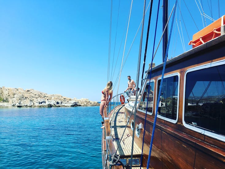 A woman standing on the side of the boat before jumping into the crystal clear water during the Sailing Boat Trip to Delos & Rhenia Island with BBQ with Greece Sailing.