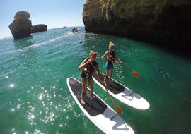 Deux femmes debouts sur un stand up paddle lors de la Balade en stand up paddle depuis la plage de Galé le long de la côte de l'Algarveavec Nautifun Galé Albufeira.