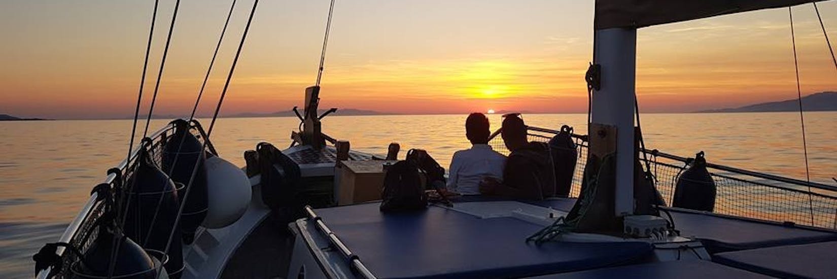 Zwei Menschen auf dem Boot von Mykonos Cruises genießen die Bootstour bei Sonnenuntergang um Mykonos.