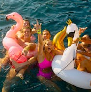 Un groupe d'amis s'amuse en nageant avec des structures gonflables sur les eaux bleues de la baie de Mykonos lors d'une balade en bateau avec le Mykonos Boat Club.