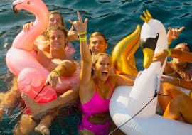 Un grupo de amigos se divierten nadando con inflables en las aguas azules de la bahía de Mykonos durante un viaje en barco de fiesta con Mykonos Boat Club.