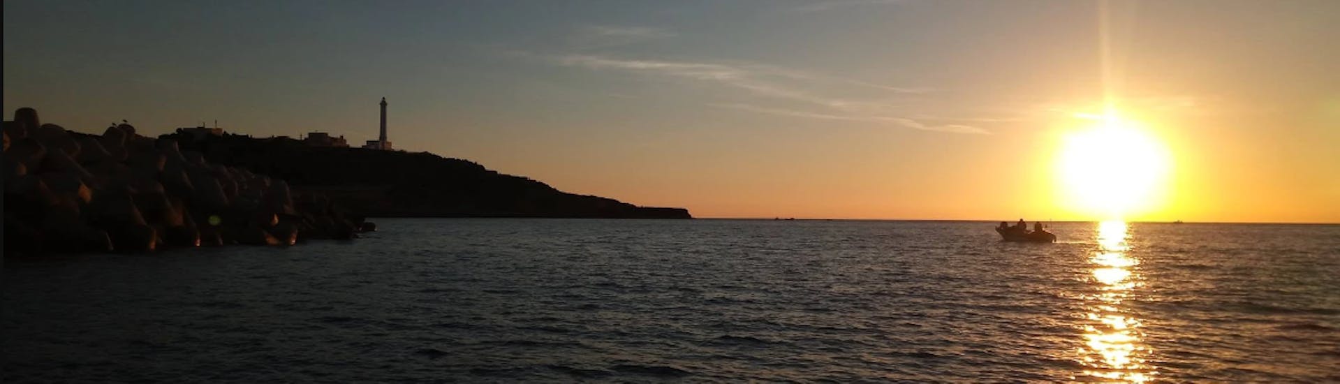 Foto van het uitzicht op de baai voor de vuurtoren van Leuca bij zonsondergang vanaf een boot van Leucos Escursioni Leuca tijdens de boottocht van Santa Maria di Leuca naar de Zeegrotten.