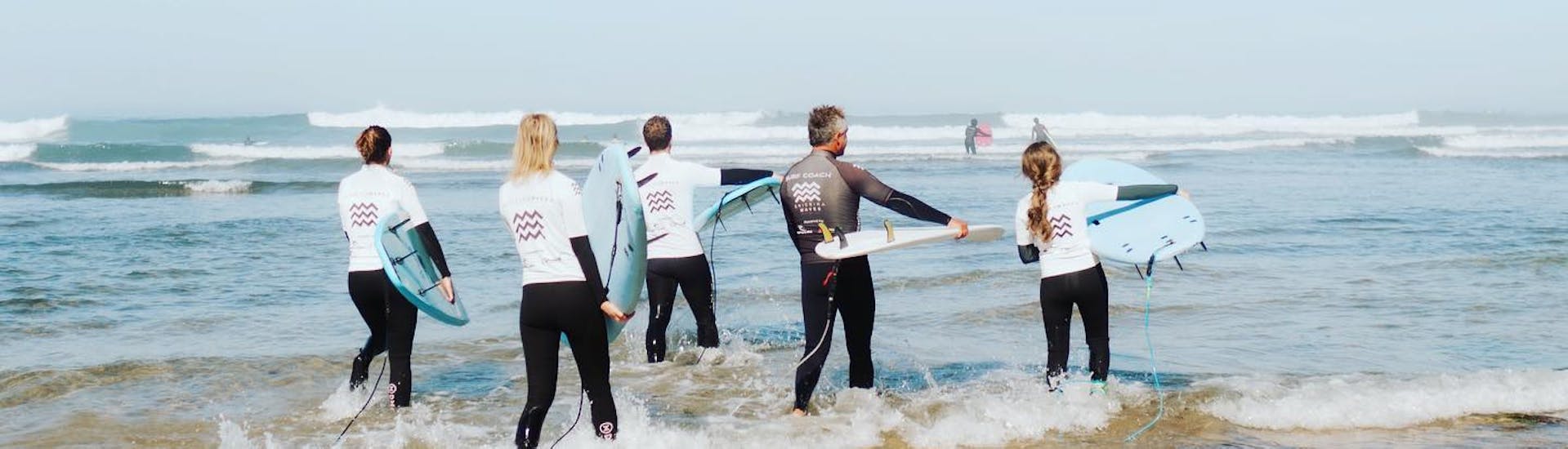 Eine Gruppe von Leuten mit ihren Surfbrettern während eines Surfkurses in Ericeira am Praia de Ribeira d'Ilhas mit der Ericeira Waves Surf School.