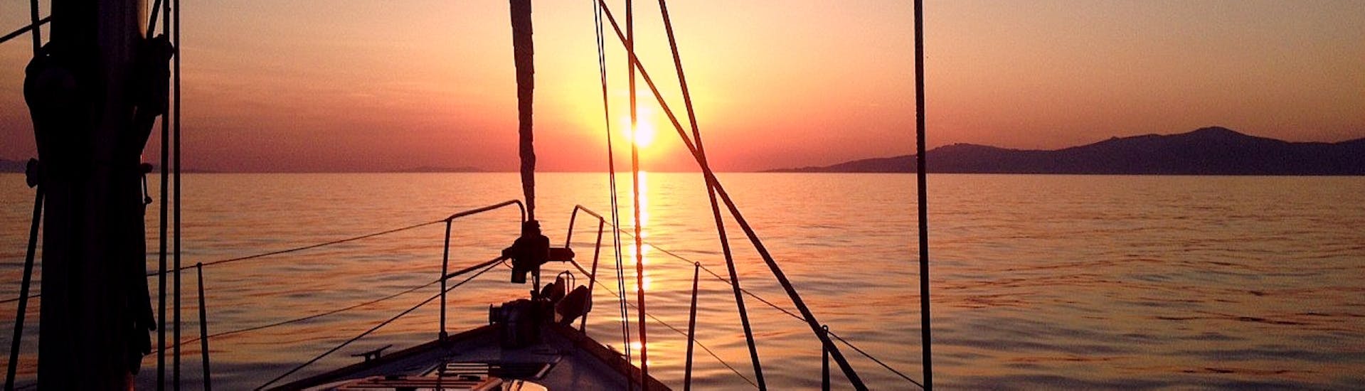 Der farbenfrohe Sonnenuntergang über dem Ägäischen Meer malt das blaue Wasser, mit einem Segelboot vor der Sonnenuntergangs-Bootstour von Mykonos nach Rhenia mit Set Sail Mykonos.