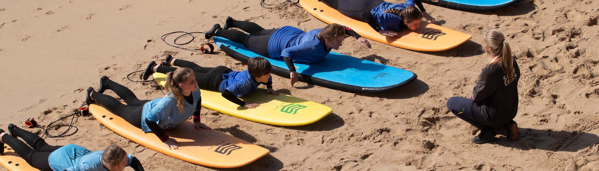 Eine Gruppe von Menschen lernt während eines Surfkurses in Ericeira am Praia do Matadouro mit dem Boardculture Surf Center das Paddeln.