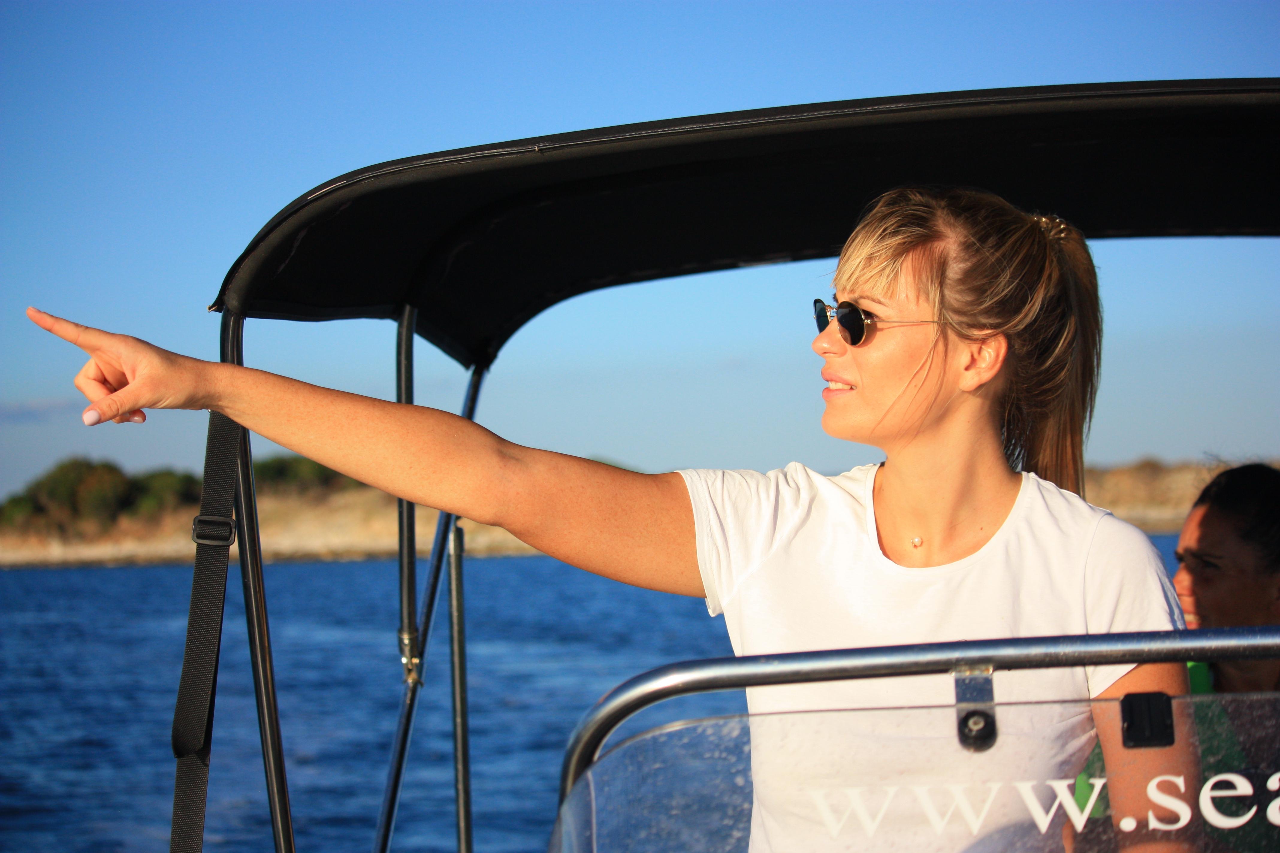 Una mujer con gafas de sol sonríe y señala hacia el mar abierto durante una excursión privada en barco al atardecer con avistamiento de delfines desde Fažana por Sea Tours Istria Fažana.