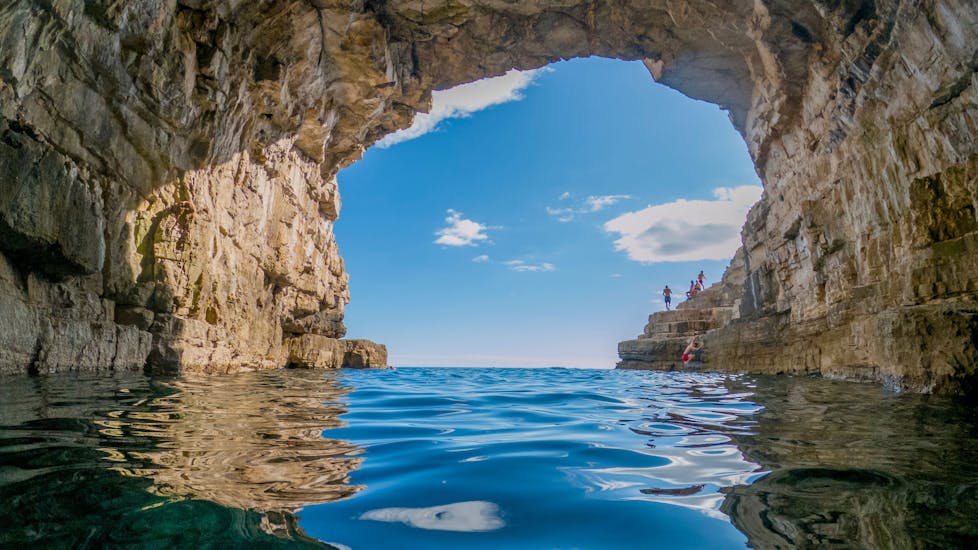 Mensen klimmen op de rotsen en zwemmen onder de grot tijdens de privé boottocht naar de Meeuwenrotsen in Pula vanuit Fažana met Sea Tours Istria Fažana.