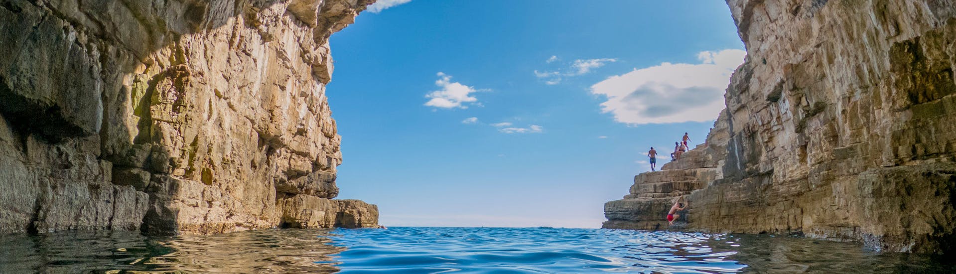 Mensen klimmen op de rotsen en zwemmen onder de grot tijdens de privé boottocht naar de Meeuwenrotsen in Pula vanuit Fažana met Sea Tours Istria Fažana.