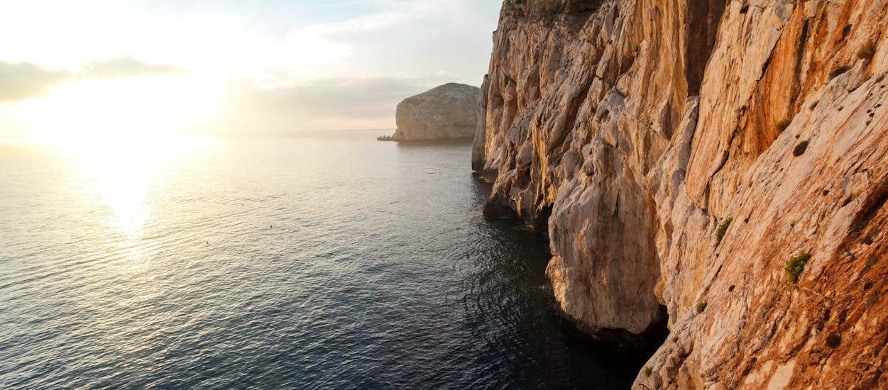 Foto de la romántica puesta de sol a la entrada de las cuevas de Neptuno tomada durante un paseo en velero desde Alghero por la costa con aperitivo al atardecer con Coral Sail Alghero.