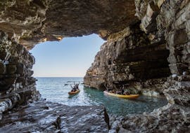Delle persone entrano in una grotta durante l'escursione in kayak alla grotta di Cape Kamenjak con snorkeling con Kayaking Premantura.