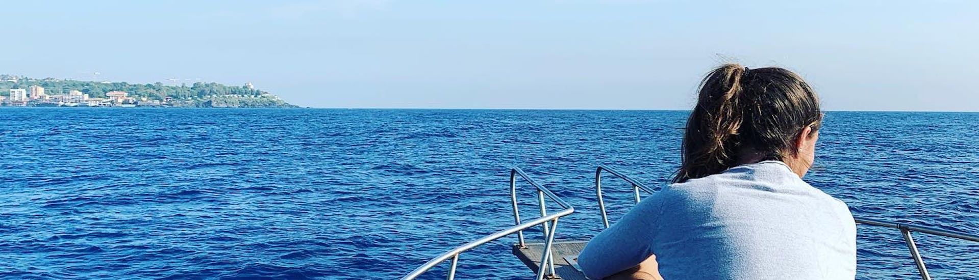 Meisje zittend op de boot van Etna & Sea Excursions Catania kijkend naar de zee tijdens de boottocht in het beschermde gebied van de Cyclops-eilanden met snorkelen.