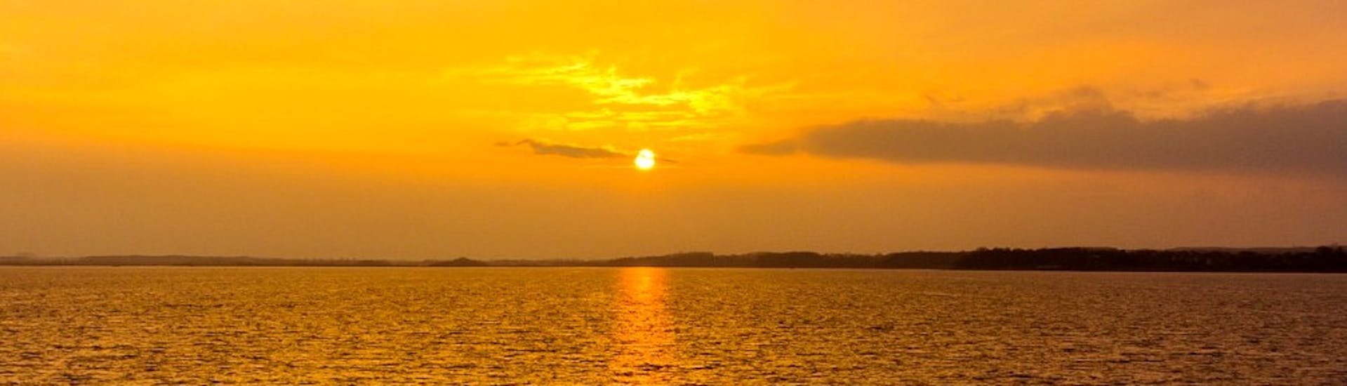 La puesta de sol sobre el Pacífico mientras pinta las aguas turquesas en un tono rojo brillante durante un viaje en barco al atardecer desde Lagos a Carvoeiro con Funtastik Tours Lagos.