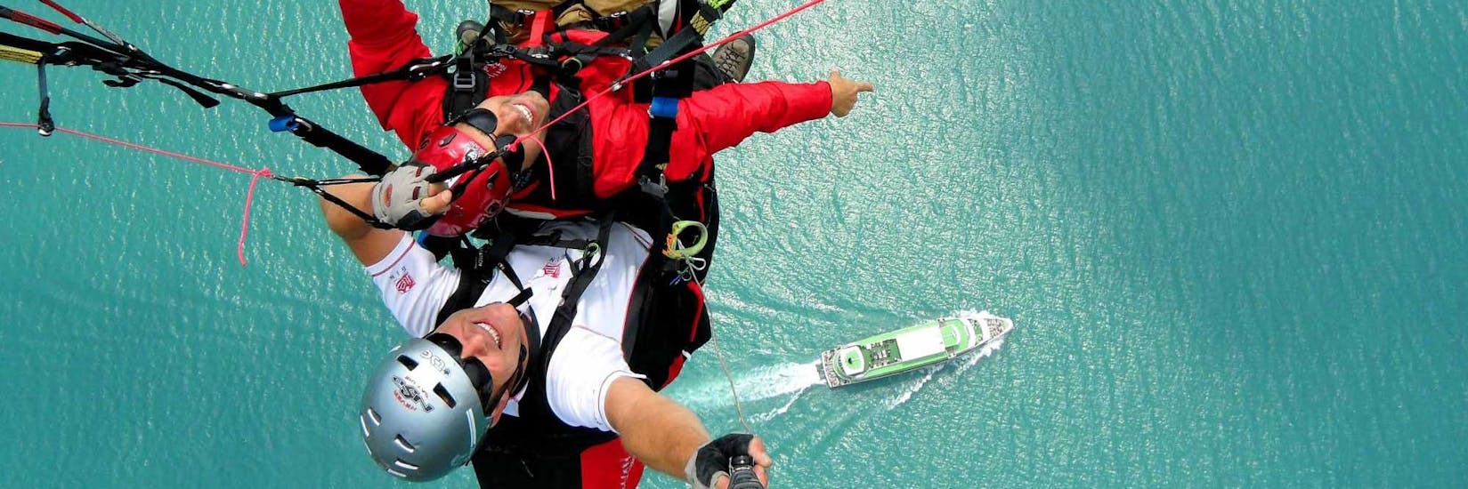 Ein Mann und sein Pilot über dem See zeigen auf ein Schiff unter ihnen während des Tandem Paragliding from Beatenberg to Interlaken with AlpinAir Paragliding Interlaken.