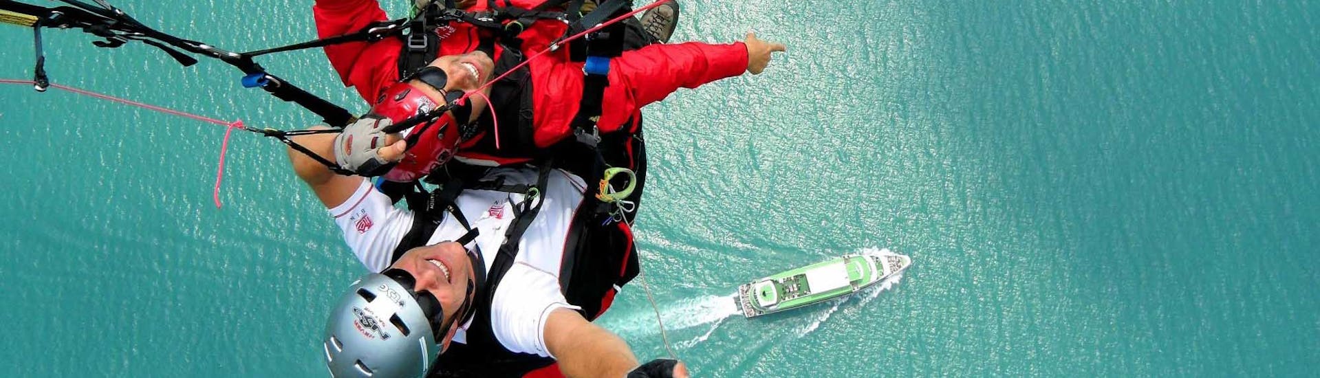 Ein Mann und sein Pilot über dem See zeigen auf ein Schiff unter ihnen während des Tandem Paragliding from Beatenberg to Interlaken with AlpinAir Paragliding Interlaken.