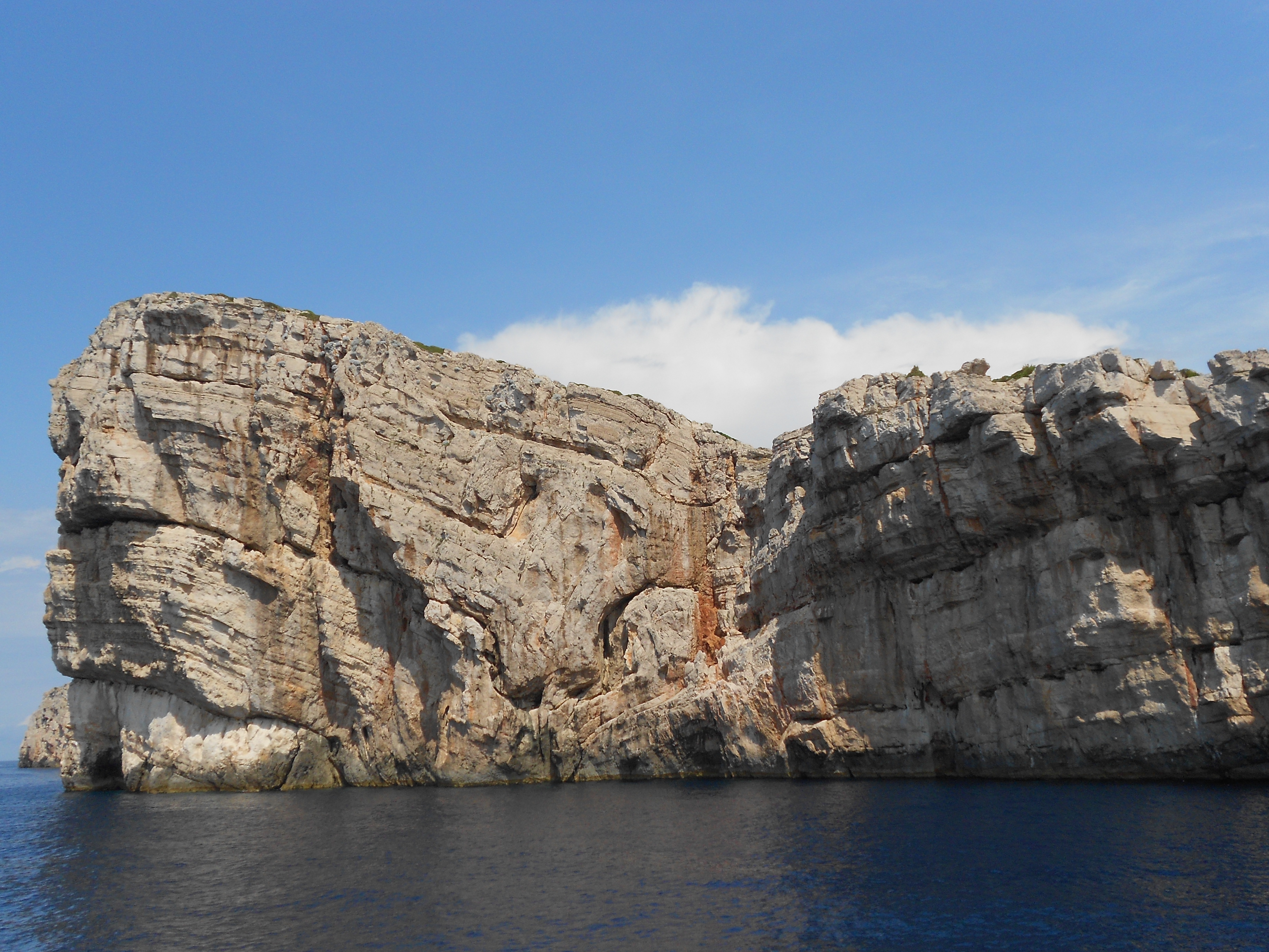 A sheer, rocky cliff rises from the deep blue sea in the Kornati National Park during a boat trip with lunch and drink by Avalon Yachting Šibenik.