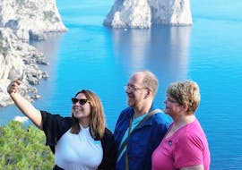 Tres personas tomándose un selfie con el fondo de los Faraglioni durante la excursión en barco por Capri con visita guiada a la isla con HP Travel Capri.
