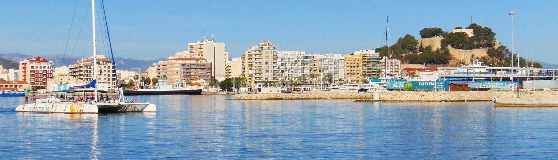 El elegante y moderno catamarán de vela ecológico navega frente al hermoso Puerto de Málaga durante un día completo de viaje en barco desde Málaga a lo largo de la Costa del Sol con Mundo Marino Costa del Sol.