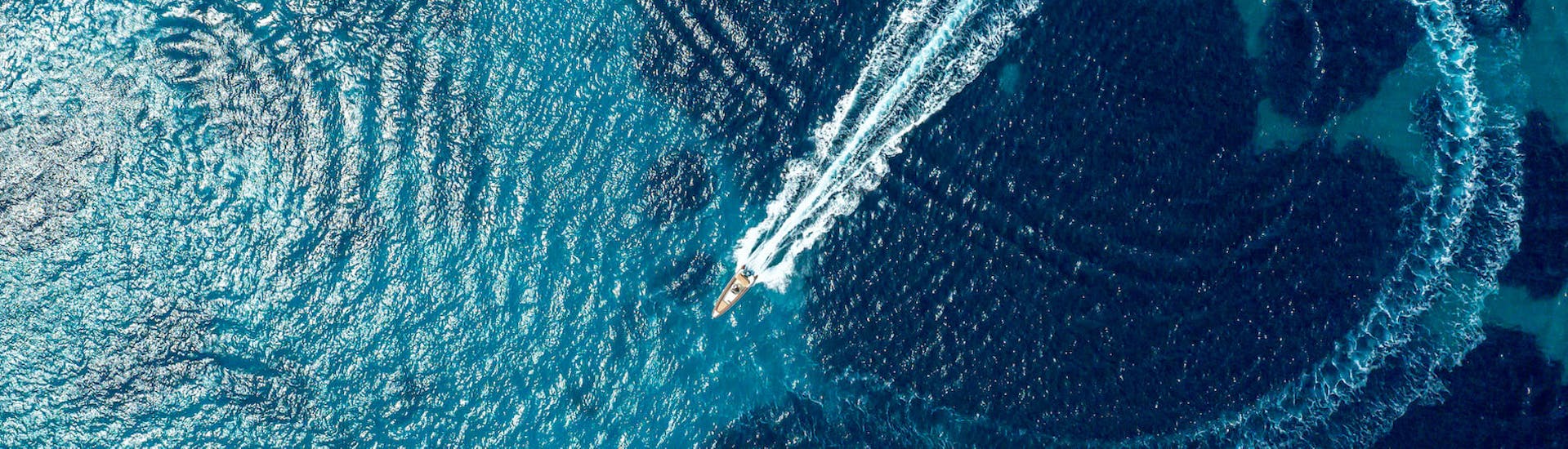 Een van de boten van Venus van Milos cruisend door de diepblauwe zee tijdens de Volle dag privé Boottocht langs de kust van Milos.