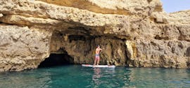 Un homme ressort d'une grotte sur sa planche de SUP pendant la balade guidée en Stand Up Paddling de Praia dos Arrifes le long de la côte avec Surf4Fun Albufeira.