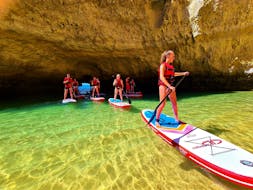 Un gruppo di persone esce da una grotta in mare sulle loro tavole da SUP durante il tour di stand up paddle da Praia de Albandeira alla grotta di Benagil con Surf4Fun Albufeira.