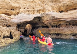 Delle persone esplorano una grotta naturale a bordo di un kayak durante il tour in Kayak alla grotta di Benagil da Praia de Albandeira con Surf4Fun Albufeira.
