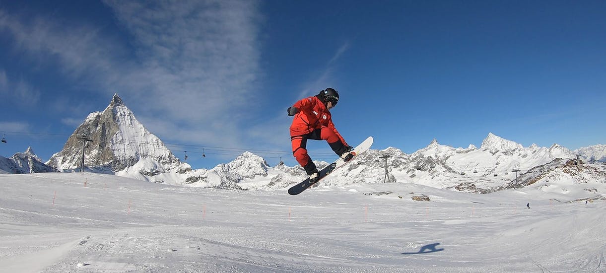 Ein Snowboardlehrer hüpft über eine Schanze vor dem Bergpanorama von Zermatt beim Privater Snowboardkurs für Kinder und Erwachsene aller Levels mit der Evolution Skischule Zermatt.