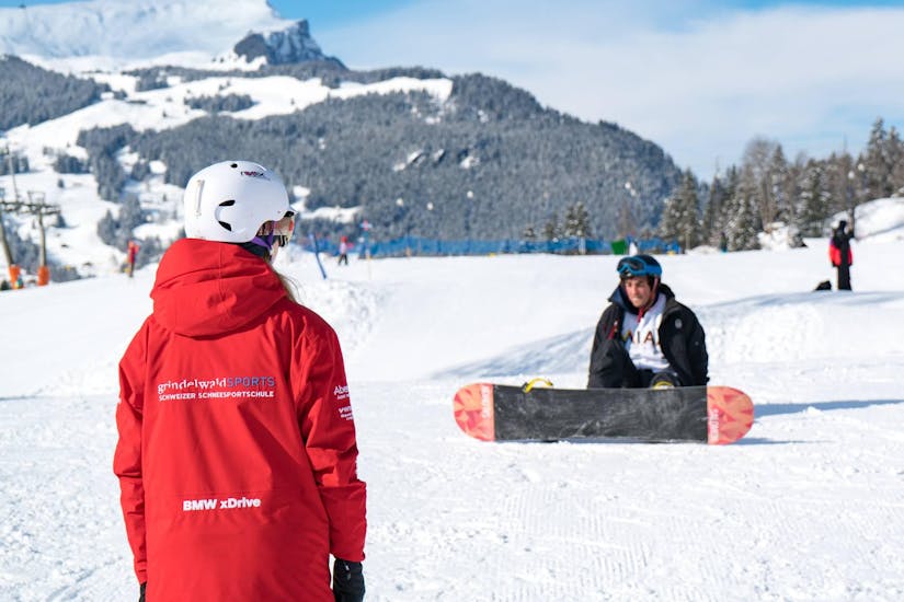 A snowboard instructor shows a participant how to stand up properly at the snowboard course + snowboard rental package for adults for beginners with the Swiss Ski School Grindelwald.