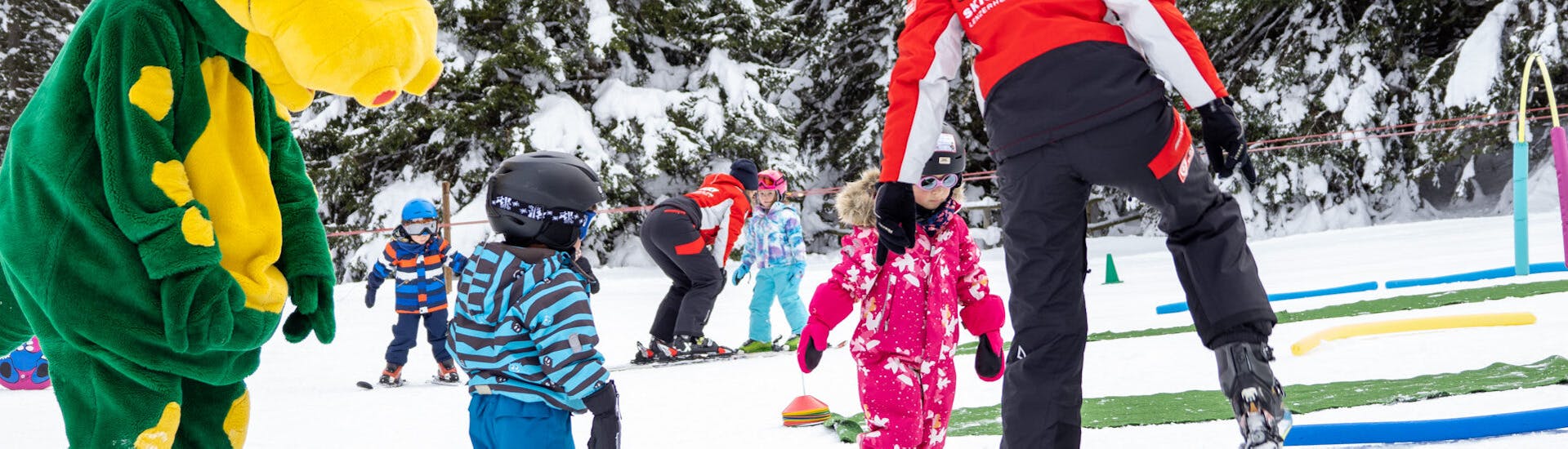 Mascotte met jonge skiër in kinderland tijdens skilessen voor kinderen bij skischool Nova.