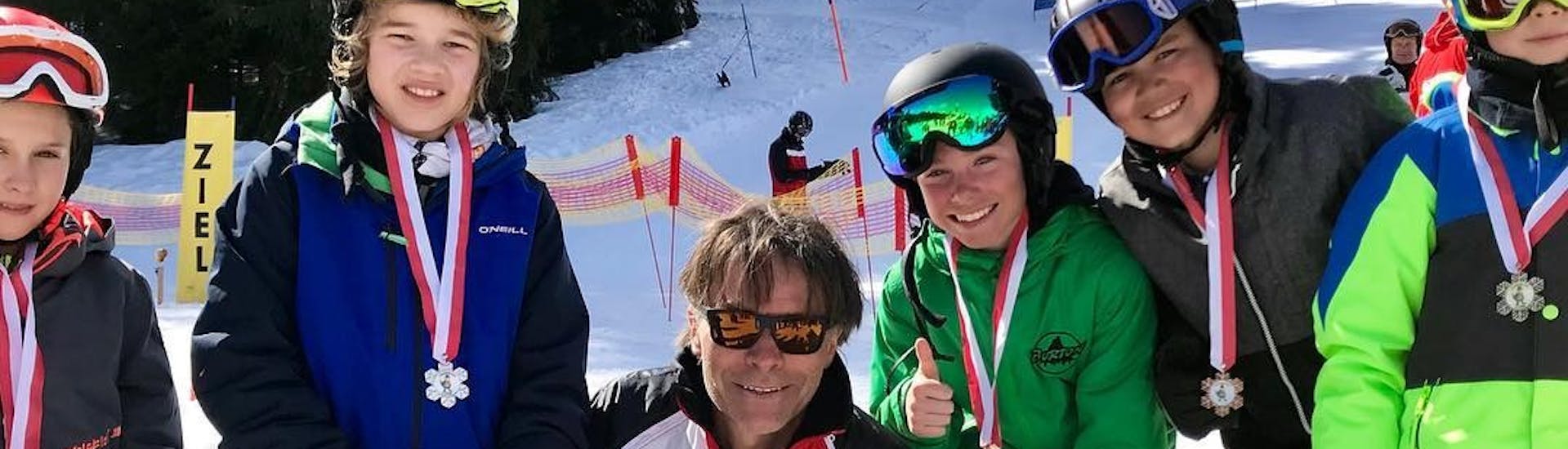 Kinderen met instructeur die hun medailles omhoog houden tijdens de kinderskilessen voor ervaren skiërs bij skischool Nova.