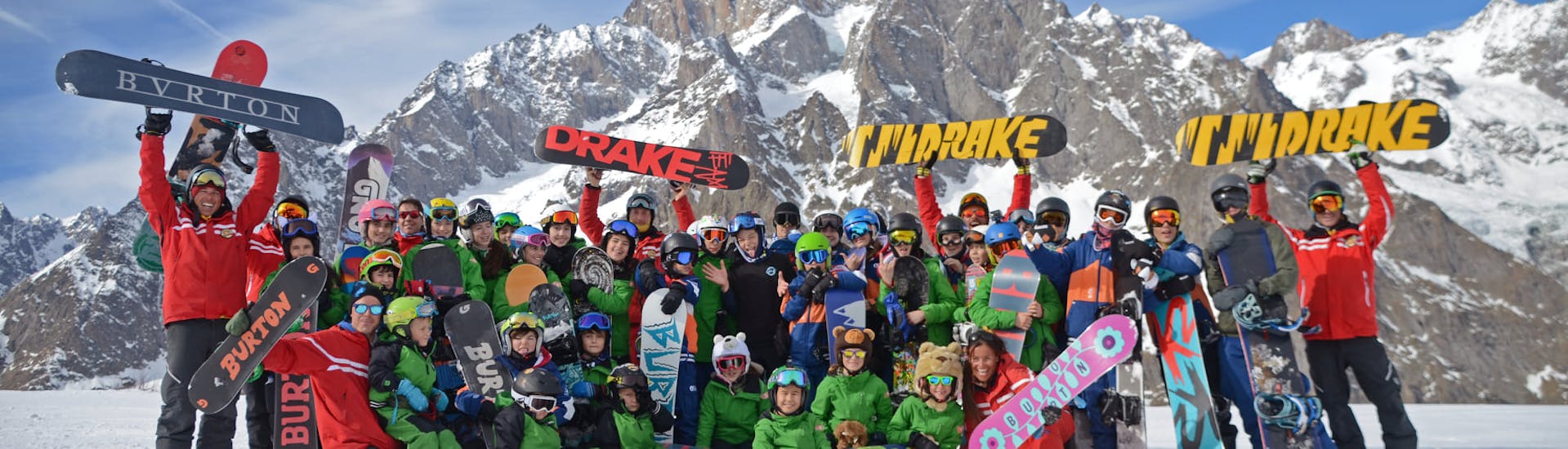 Foto di un gruppo di persone che posano davanti alla macchina fotografica con i loro maestri della Scuola di Sci Monte Bianco Courmayeur durante le Lezioni di snowboard (dai 5 anni) per tutti i livelli.