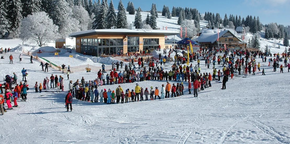 Kinderen in een kring die zich opwarmen voor de kinderskilessen (vanaf 3 j.) voor beginners bij Schneesportschule ON SNOW Feldberg.
