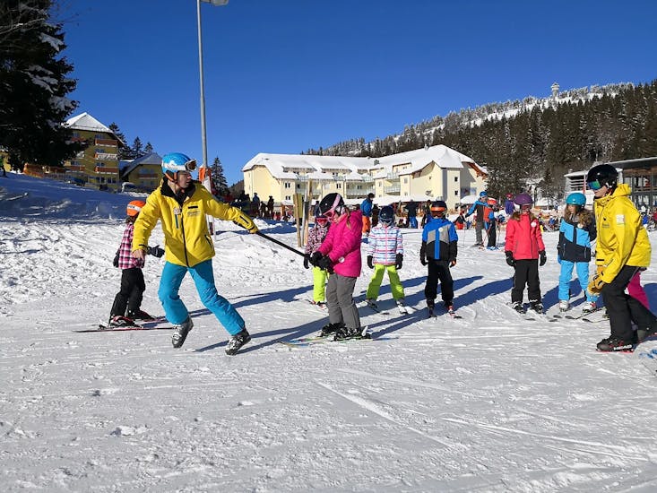 Een skileraar trekt een kind met zijn stokken en toont haar de juiste vorm tijdens de kinderskilessen (4-13 jr) voor alle niveaus bij Schneesportschule ON SNOW Feldberg.