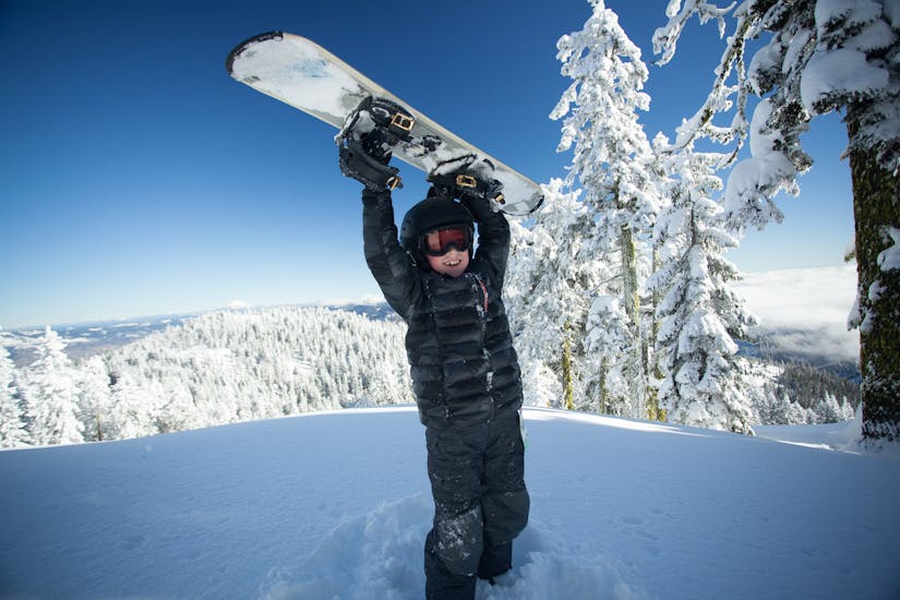 Ein Snowboarder hebt sein Board in die Luft beim Snowboardkurs für Kinder (ab 7 J.) & Erwachsene aller Levels mit der Schneesportschule ON SNOW Feldberg.