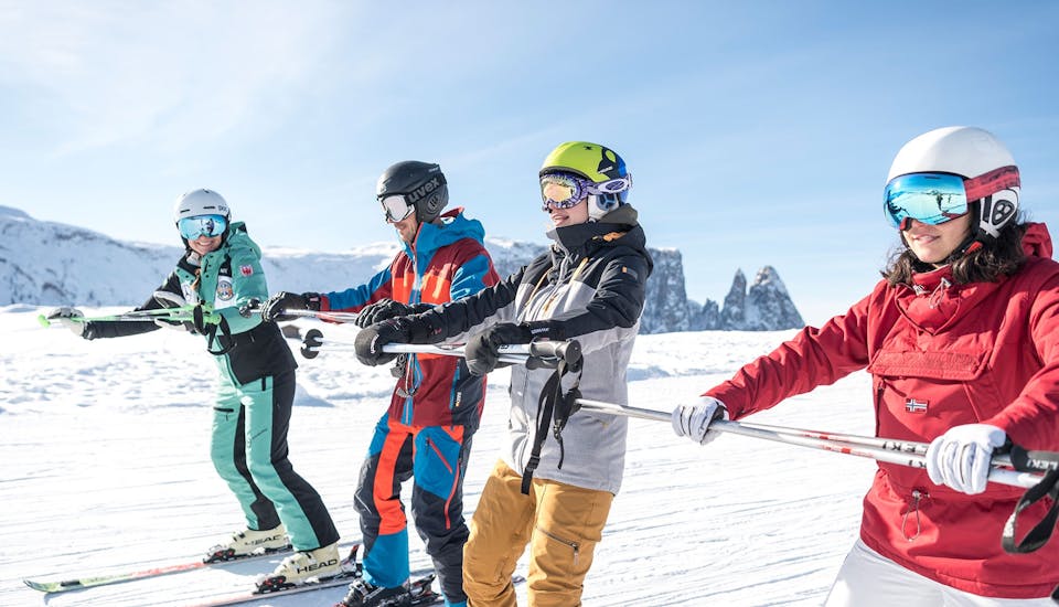 Volwassenen houden zich vast aan een stang tijdens de skilessen voor volwassenen voor alle niveaus met skischool Schlern 3000.