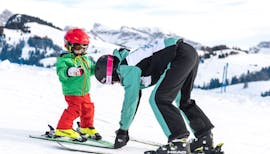 Un maestro di sci mette gli sci di un bambino a spazzaneve durante le Lezioni private di sci per bambini per tutti i livelli con Skischool Schlern 3000 Alpe di Siusi.