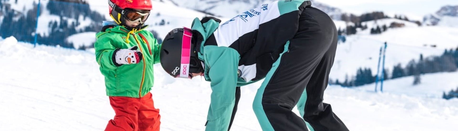 Un maestro di sci mette gli sci di un bambino a spazzaneve durante le Lezioni private di sci per bambini per tutti i livelli con Skischool Schlern 3000 Alpe di Siusi.