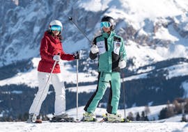 Il maestro di sci indica una direzione con i bastoncini durante la lezione di sci private di sci per adulti per tutti i livelli con Skischool Schlern 3000 Alpe di Siusi.
