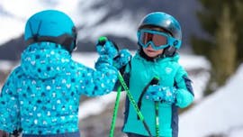 Deux enfants se tapent dans la main pendant les cours de ski pour enfants débutants (3-5 ans) de l'école de ski Bergsport JA Oberstdorf.