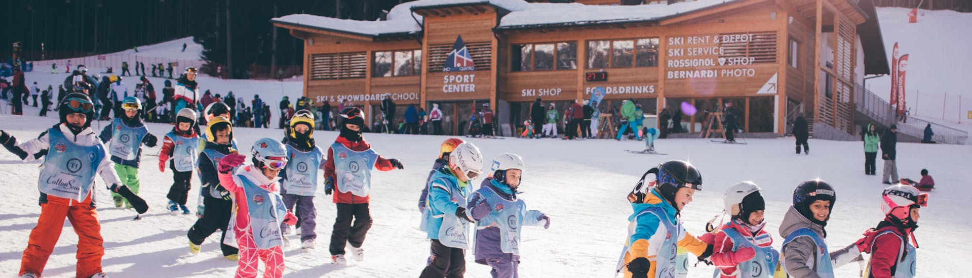 Alcuni bambini passeggiano di fronte all'ufficio della Scuola di Sci Marilleva durante le Lezioni di sci per bambini (3-12 anni) per principianti.