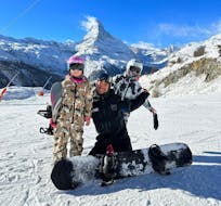 Un moniteur de PDS Snowsport pose avec deux snowboardeurs devant le mont Cervin pendant leur Cours particulier de snowboard pour Tous niveaux