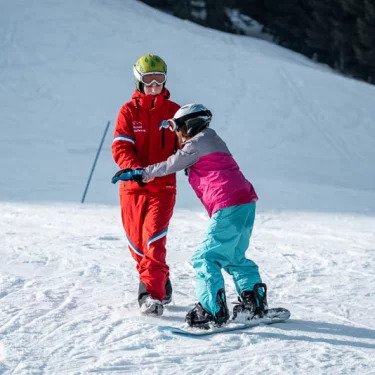 A snowboard instructor shows a student how to stand properly on the board at the snowboarding lessons for children (from 8 years) & adults of all levels with the Nesselwang Ski School.
