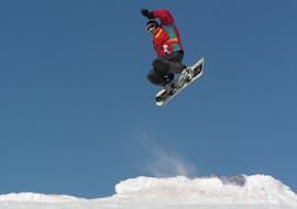Snowboarder springt op de piste tijdens de privéles snowboarden voor kinderen en volwassenen op alle niveaus bij G&S sneeuwsportschool Mitterdorf.