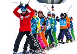 Een groep kinderen poseert voor de camera met hun instructeur tijdens de skilessen voor kinderen (5-12 jaar) voor alle niveaus met Scuola di Sci Pila.