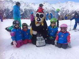 A group of young skiers take a photo with the mascot Bobi at Bobi's Snowkindergarden (2,5-4 y.) for First Timers with Ski School Grächen - Zenklusen Sport.