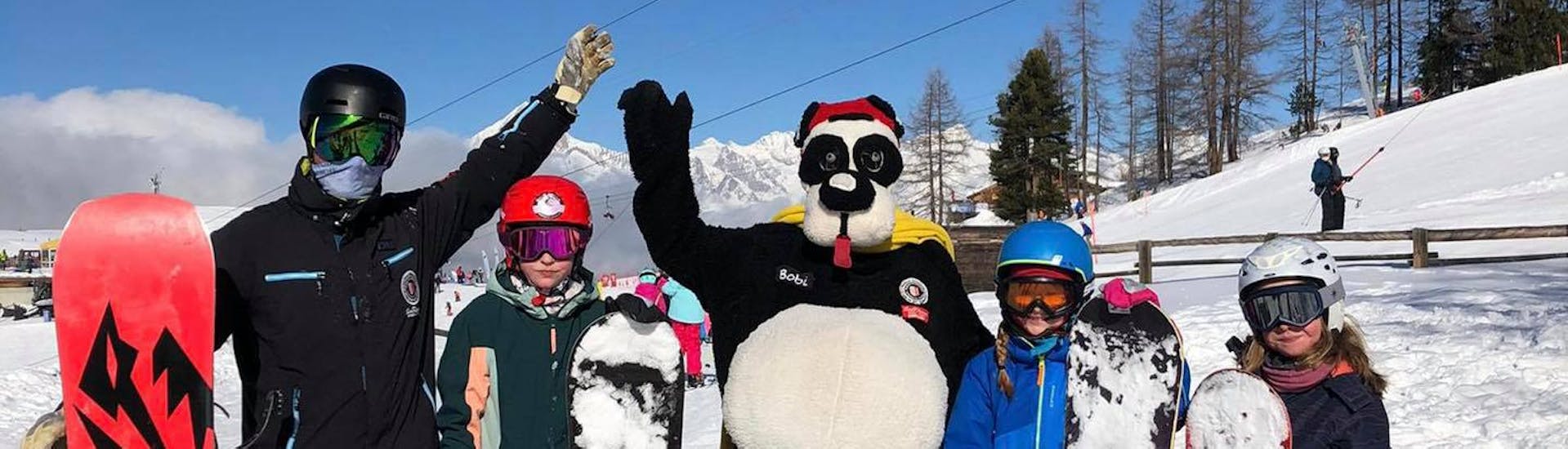 Eine Gruppe Snowboarder wird vom Maskottchen Bobi besucht beim Snowboardkurs für Kinder & Erwachsene (ab 4 J.) für Anfänger mit der Skischule Grächen - Zenklusen Sport.