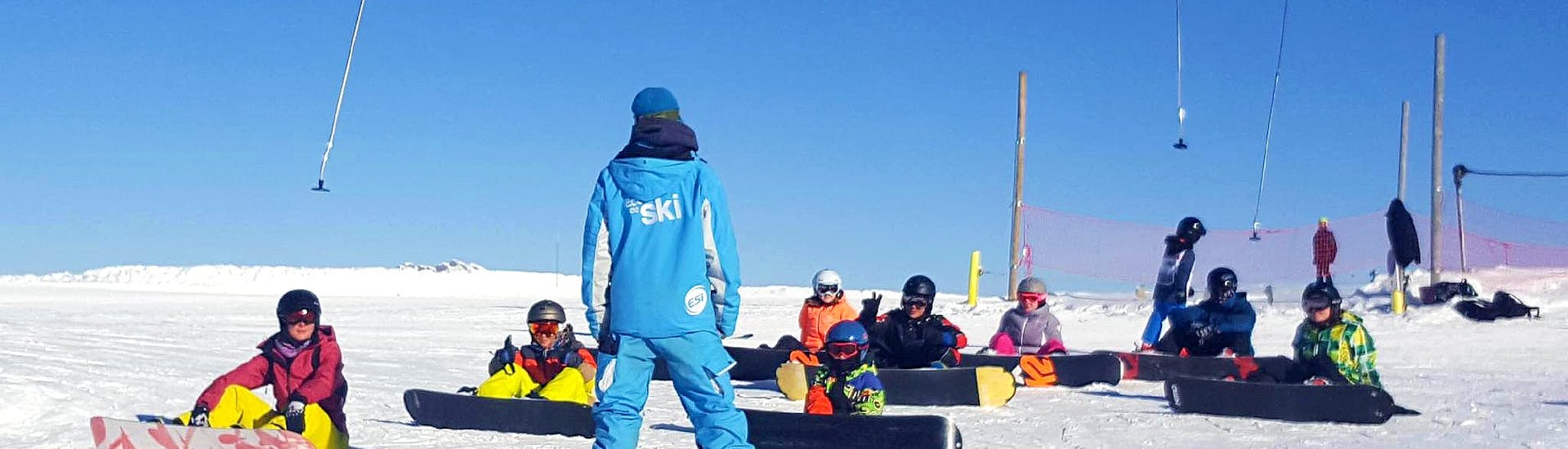 Die Schüler hören ihrem Lehrer während des Snowboardkurses für Kinder und Erwachsene für alle Levels bei ESI Grand Massif aufmerksam zu.